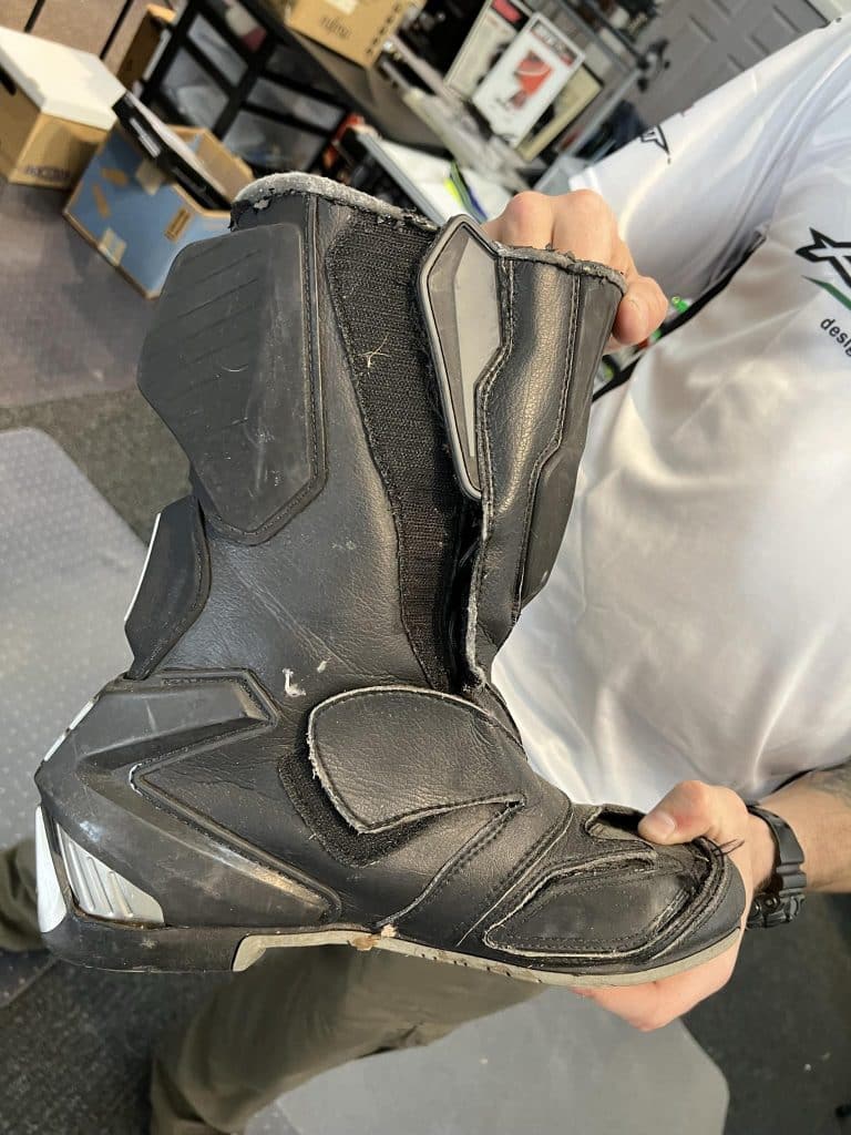 A 2005 AGVSPORT Laguna race boot, weathered and marked with signs of a crash and fatigue in high-friction areas. Despite its nearly two decades of use, this boot proved its worth by effectively safeguarding the rider during a high-speed crash exceeding 80 mph.
