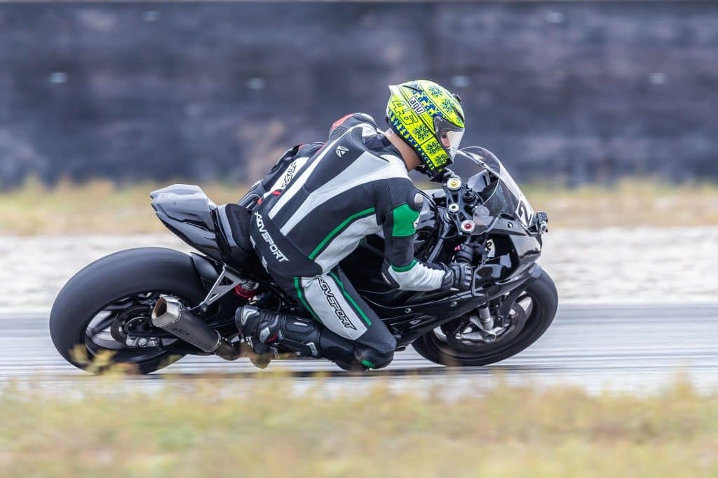 Denis Grachev, at it again, demonstrating proper track cornering technique on a BMW S1000RR dressed in AGVSPORT Laguna one-piece suit, AGVSPORT race boots, and the FIM-homologated AGV GP R helmet. Leaning off the bike lowers the center of gravity by bringing the leg closer to the surface and puts pressure on the opposite leg to grip the bike.