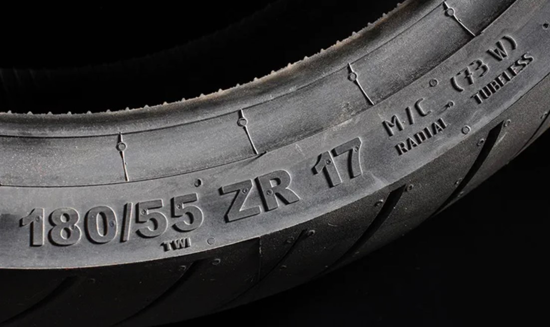 In this image, you see a high-performance 180/55 ZR17 (73W) metric motorcycle tire size. The 180mm width and 55% profile height (99mm) contribute to its specifications. The '17' signifies a 17-inch rim size, and the '73W' indicates the speed and load rating, which translates to a capacity of 365kg (805lbs.) and a maximum speed of 168mph (270km/h). The presence of brackets around the rating (73W) suggests the tire is capable of speeds beyond the specified figure. Conversely, if there were no brackets, the rating would denote the maximum allowable speed. The 'M/C' designation confirms the tire is designed for motorcycle use. The rotation direction is also evident; installing the tire incorrectly could result in a failed MoT for your bike.